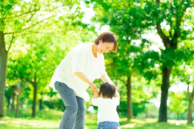 子どもが歩く練習をし、母親が両手をとって寄り添う様子